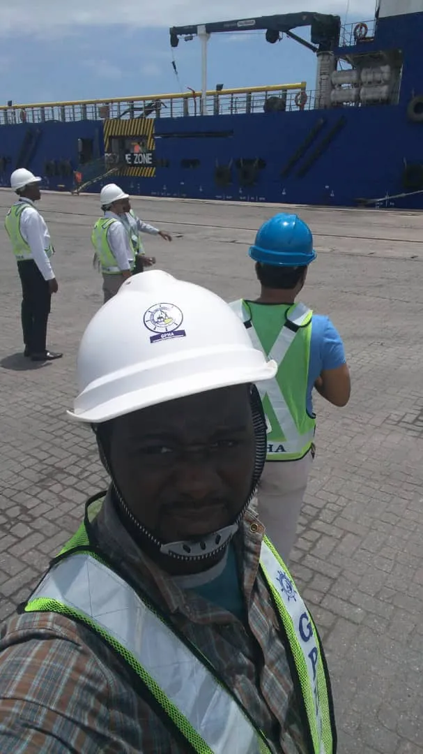 Zroni's founder in a hard hat on the quay at Tema port, cargo vessel at berth behind him